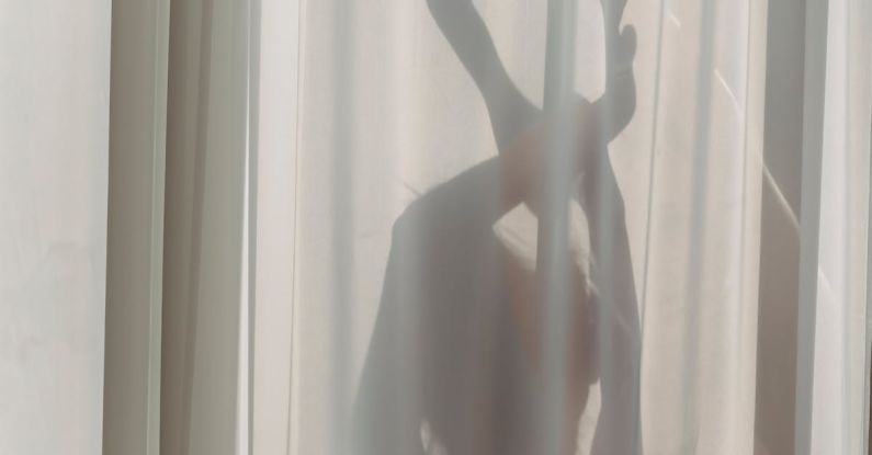 Translucent Materials - Shadow of anonymous female dancer performing sensual movements behind translucent white curtains in sunlight