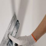 DIY Projects - Crop anonymous male worker in gloves holding putty knife while working at home