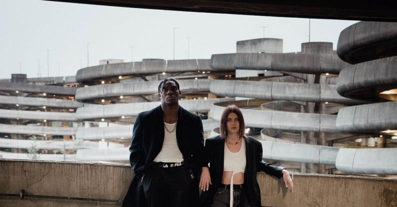 Self-healing Concrete - Full body of young confident woman and black man in trendy outfits leaning on concrete wall in multistory parking garage against urban background